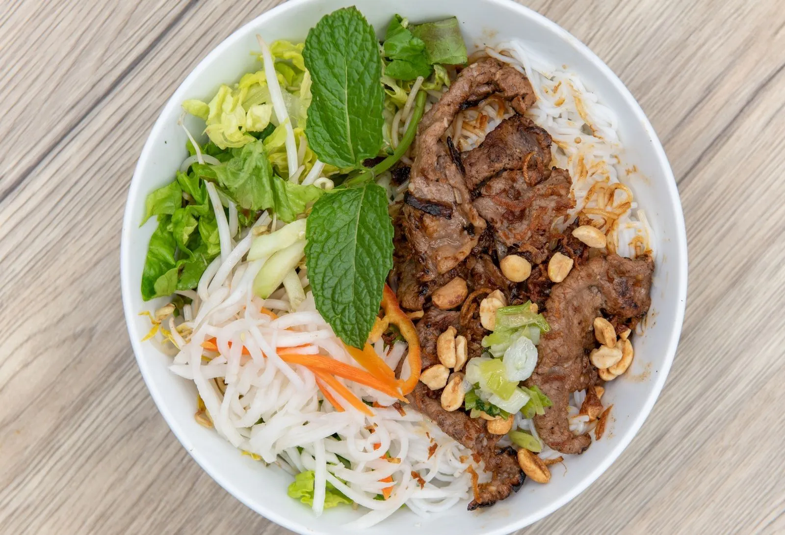 Bowl of grilled beef vermicelli noodle salad with mint, peanuts and fresh greens at Pho Kitchen, a Vietnamese Restaurant in San Jose